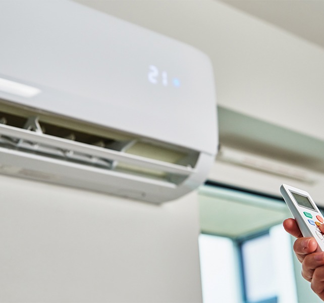 Main qui pointe une thermopompe Moovair avec une télécommande.